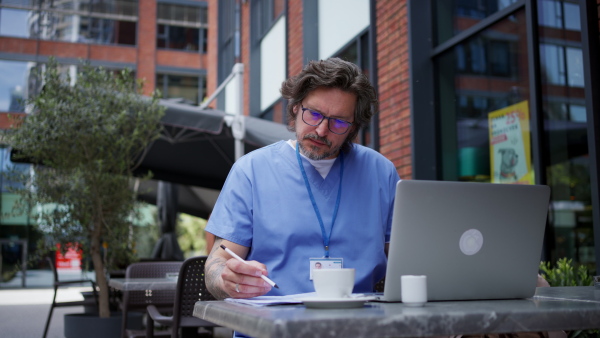 Doctor drinking coffee in coffee shop, working on laptop. Mental health and life balance for a healthcare worker. Telemedicine consultation online.