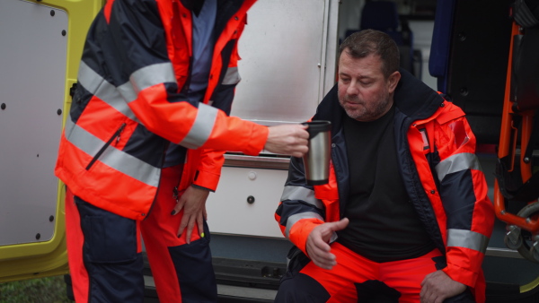 Rescuers having break in front of an ambulance car, talking and drinking coffee.