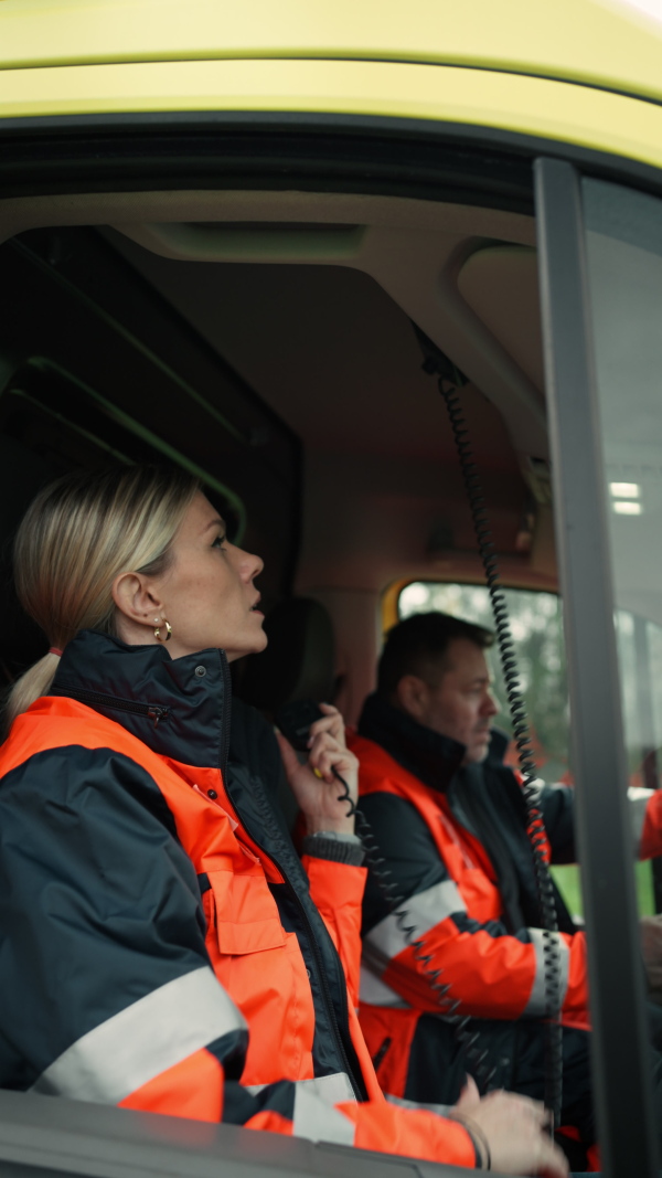 Vertical video of young woman doctor sitting and talking in to walkie-talkie in ambulance car.