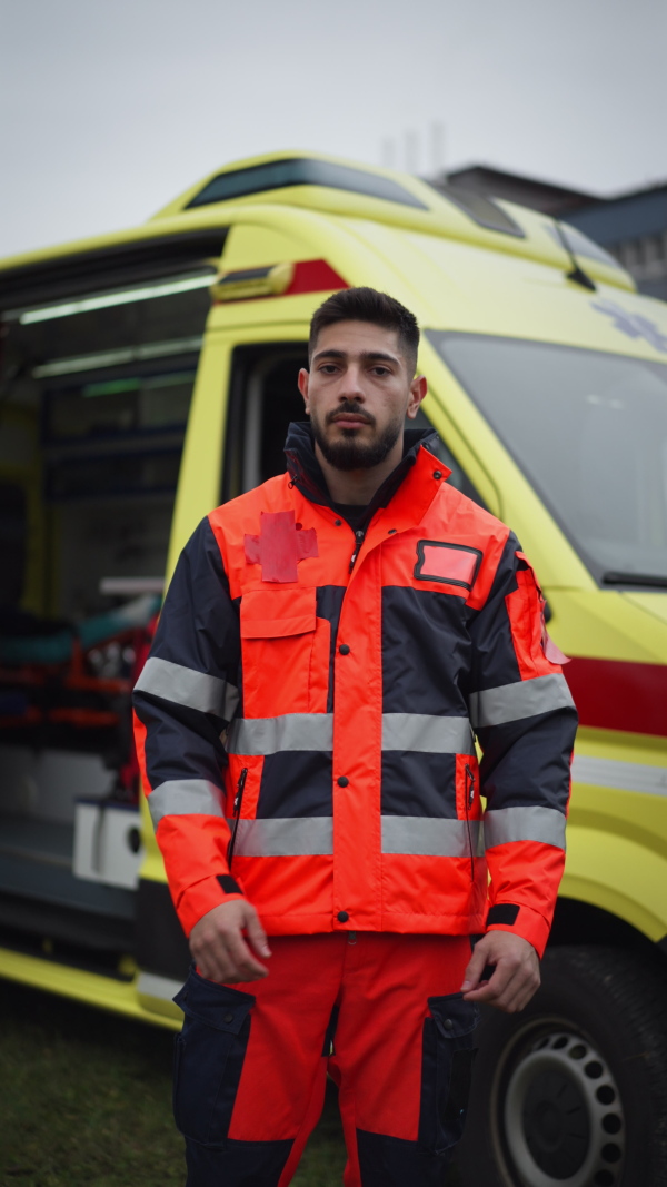 Vertical video of a young man doctor standing in front of ambulance car.