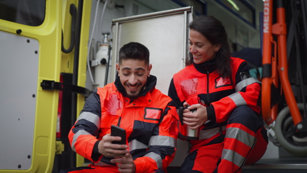 Rescuers having break in front of an ambulance car, talking and drinking coffee.