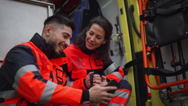 Rescuers having break in front of an ambulance car, talking and drinking coffee.