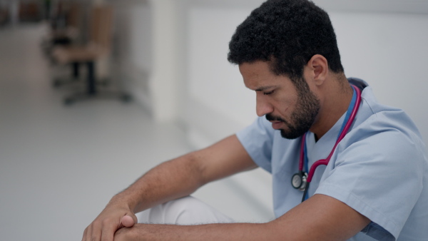 High angle view of tired doctor, sitting at a hospital corridor.