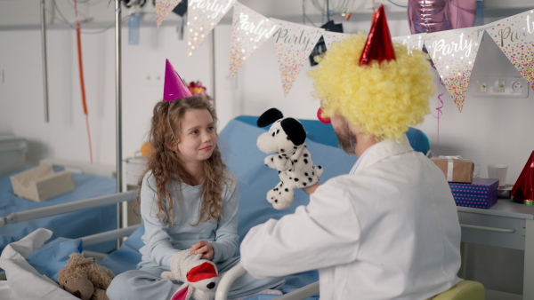 Happy doctor with clown red noses celebrating birthday with little girl in a hospital room.