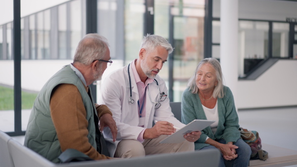 Mature doctor talking with the senior patients at hospital corridor.