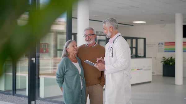 Mature doctor talking with the senior patients at hospital corridor.