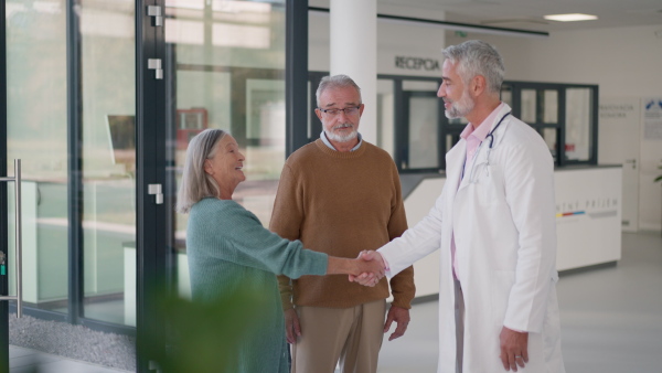 Mature doctor talking with the senior patients at hospital corridor.