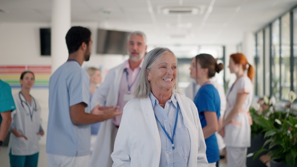 Elderly woman doctor at hospital corridor, smiling and looking at camera.