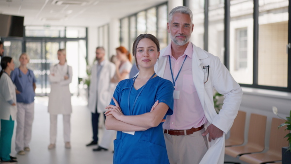 Mature doctor posing with his young nurse in hospital corridor, concept of team work.