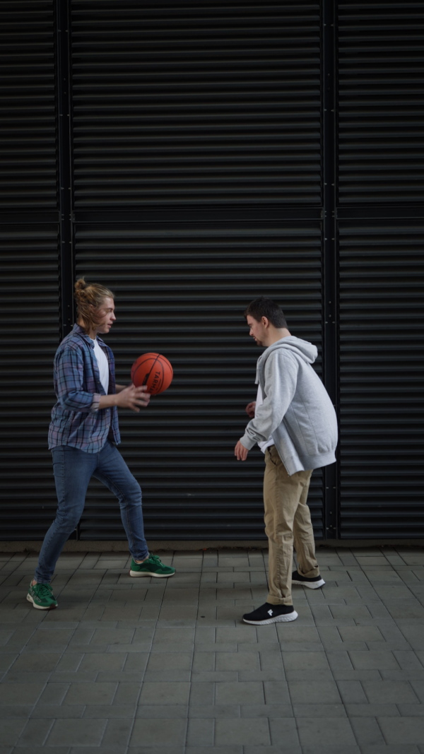 Vertical video of man with down syndrome playing basketball outdoor with his friend. Concept of friendship and integration people with disability into the society.