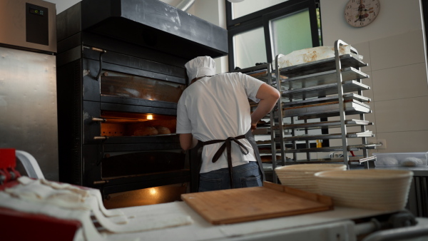 Happy young baker with fresh bread, in a bakery.