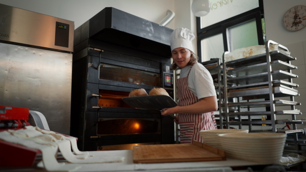 Happy young baker with fresh bread, in a bakery.