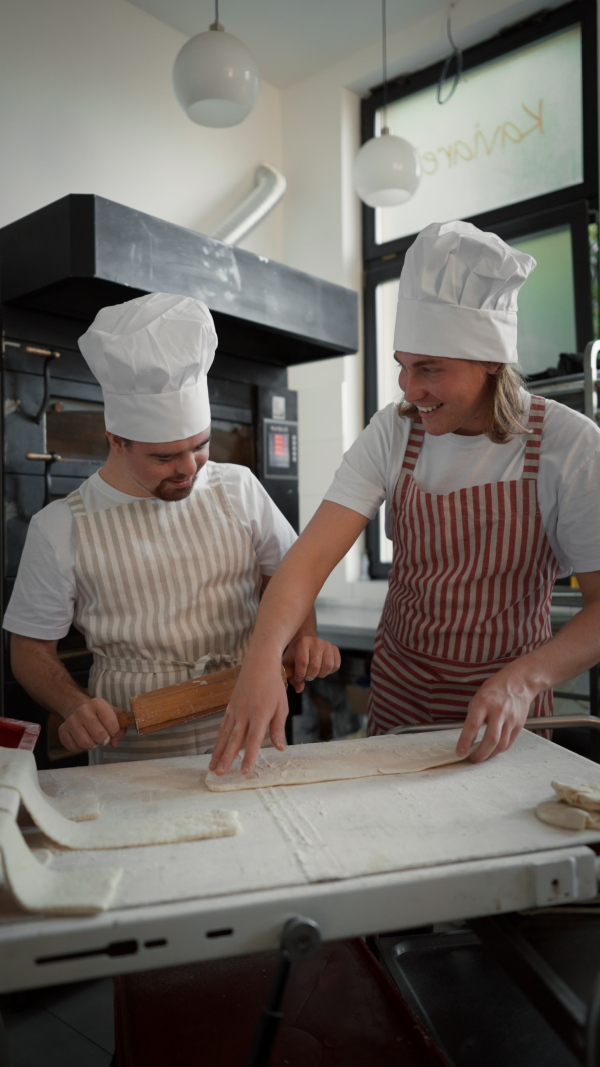 Vertical video of a man with down syndrom helping prepair bread in a bakery with his colleague. Concept of integration people with disability into society.