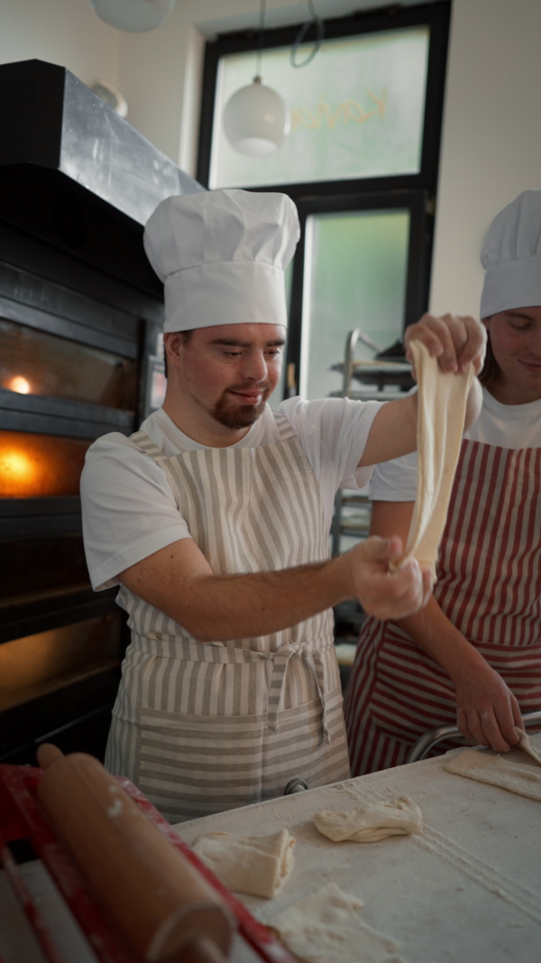 Vertical video of a man with down syndrom helping prepair bread in a bakery with his colleague. Concept of integration people with disability into society.