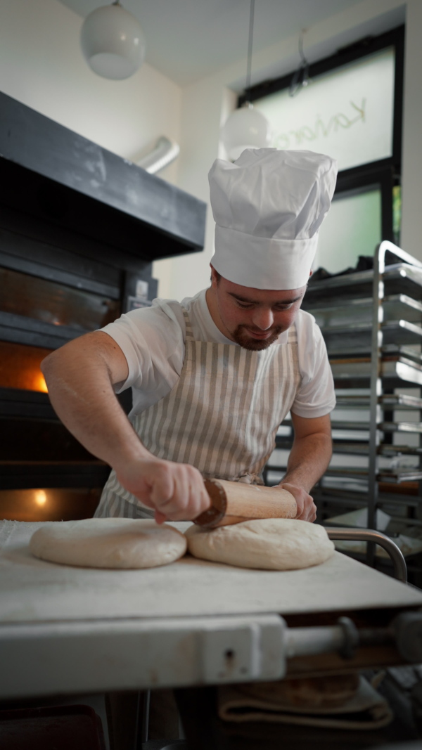 Vertical video of a young baker with down syndrome preparing pastries in bakery. Concept of integration people with a disabilities into society.