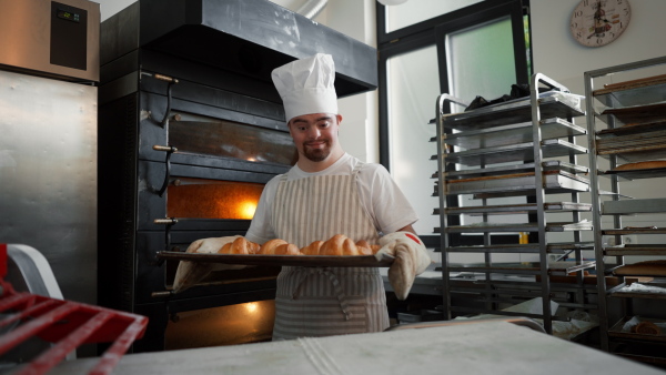 Video of young baker with down syndrome preparing pastries in bakery. Concept of integration people with a disabilities into society.