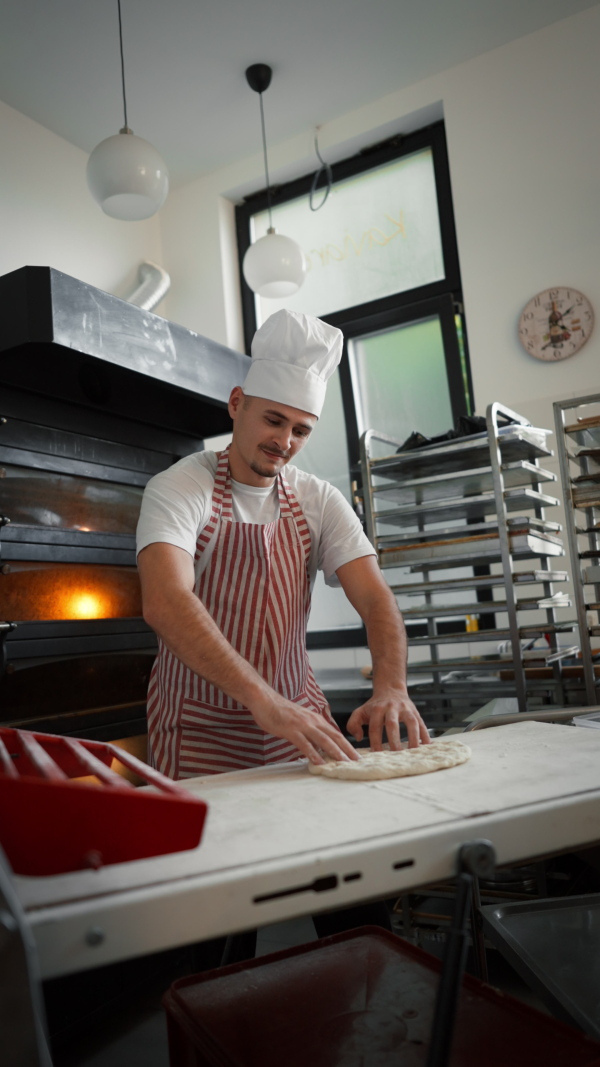 Vertical video of young baker with down syndrome preparing pastries in bakery. Concept of integration people with a disabilities into society.