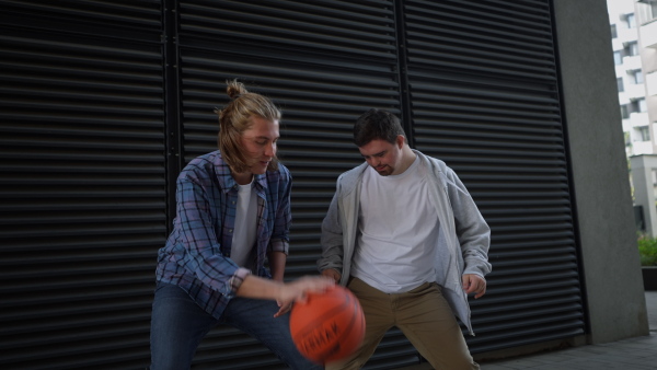 Man with down syndrome playing basketball outdoor with his friend. Concept of friendship and integration people with disability into the society.