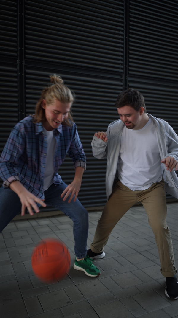 Vertical video of man with down syndrome playing basketball outdoor with his friend. Concept of friendship and integration people with disability into the society.