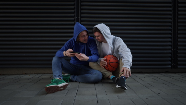 Man with down syndrome resting during basketball playing outdoor with his friend. Concept of friendship and integration people with disability into a society.