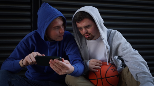 Man with down syndrome resting during basketball playing outdoor with his friend. Concept of friendship and integration people with disability into a society.