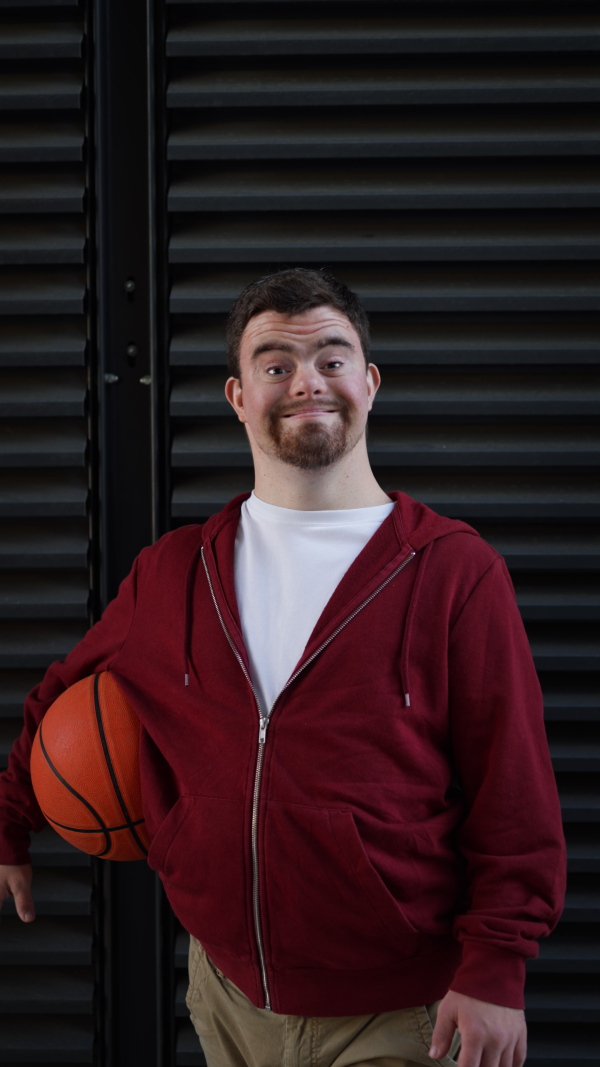 Vertical video of young man with down syndrom holding a basketball ball.