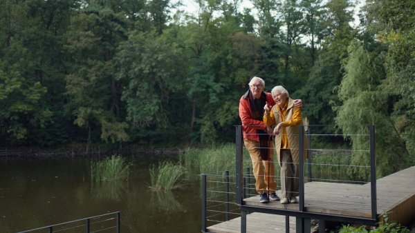 Happy senior couple at autumn walk near a lake, having break.