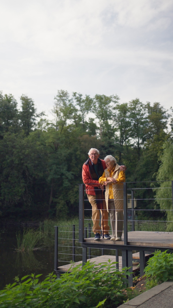 Happy senior couple at autumn walk near a lake, having break. Vertical footage.