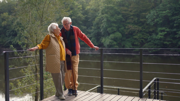 Happy senior couple at autumn walk near a lake, having break.