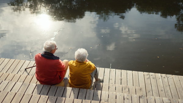 Happy senior couple at autumn walk near a lake, having break,sitting at pier.