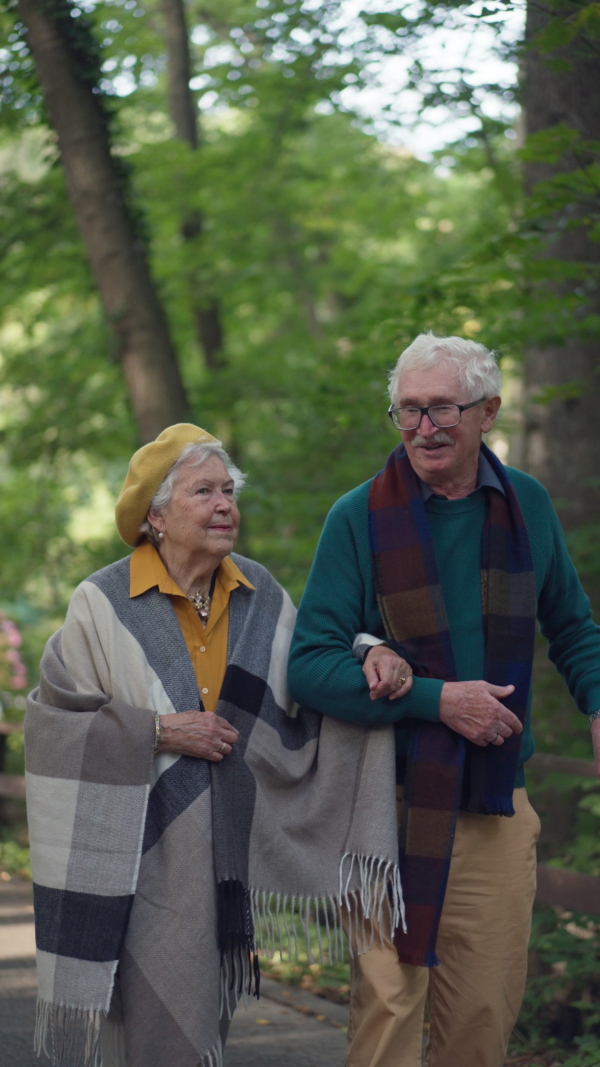 Happy senior couple in autumn clothes walking in park together. Vertical footage.