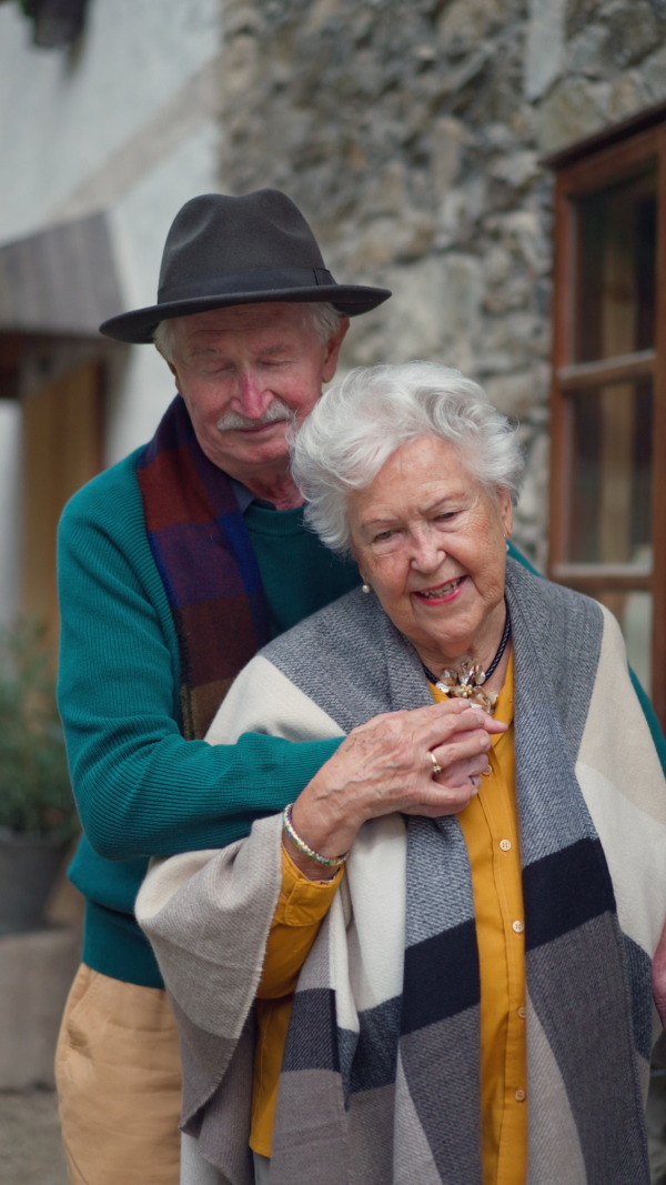 Happy senior couple posing near their old countryside house. Vertical footage.