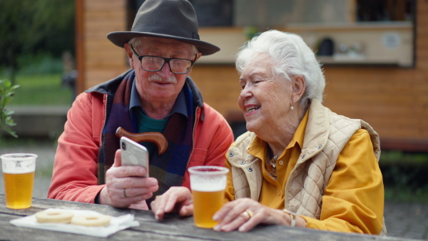 Happy senior couple in forest buffet resting after walk, having a beer and looking at smartphone.