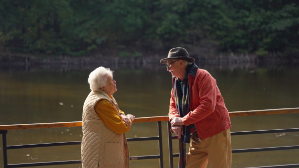 Happy senior couple at autumn walk near a lake, having break.