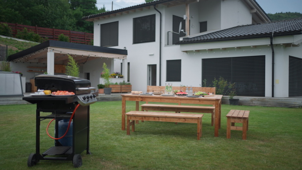 Grill with prepared meat and table with lots of food in garden, in front of house, prepared for garden party, barbecue. Nobody.