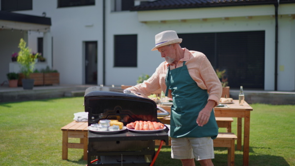 Senior man grilling outside on the backyard in summer during garden party.