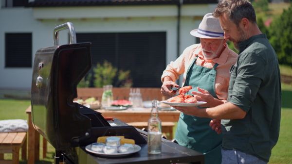 A senior father with adult son grilling outside on backyard in summer family during garden party