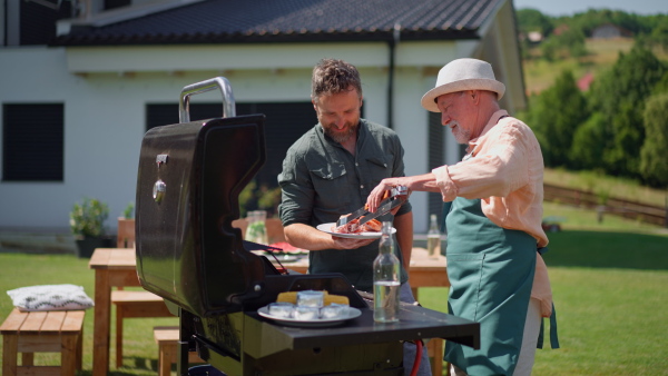 A senior father with adult son grilling outside on backyard in summer family during garden party