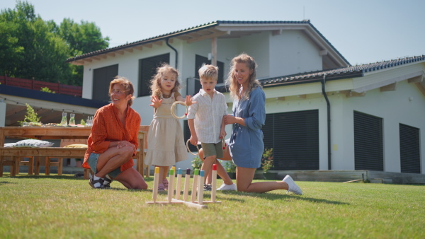 A multi generation family playing throw a ring game when grilling outside on backyard in summer at garden party.