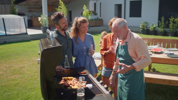 A multi generation family grilling outside on backyard in summer during garden party