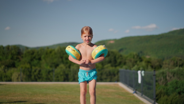 A hjappy kid having fun when jumping to swimming pool with inflatable armbands. Summer outdoor water activity for kids.