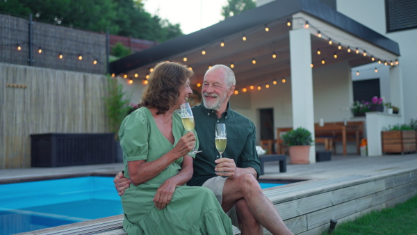 A man with his wife celebrating birthday and toasting with wine near backyard pool.