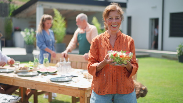 A happy senior woman serving salad at multi generation garden party in summer.