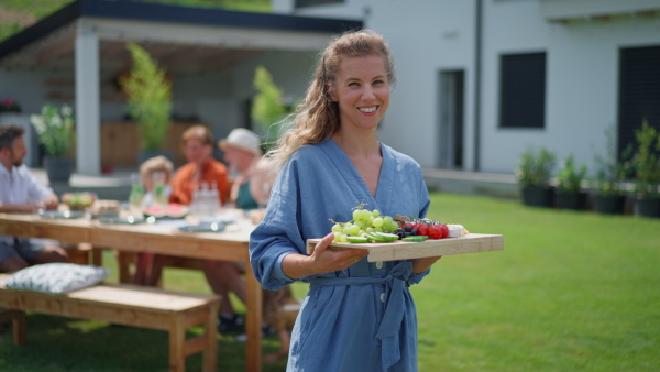 A happy young woman serving salad at multi generation garden party in summer.