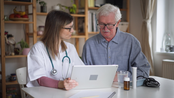 A healthcare worker or caregiver visiting senior man indoors at home, explaining medicine dosage.