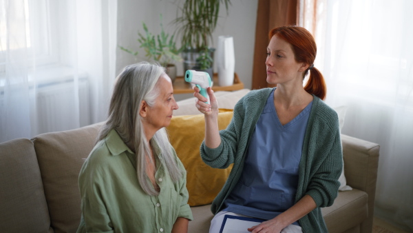 Nurse measuring body temperature to senior woman at her home.