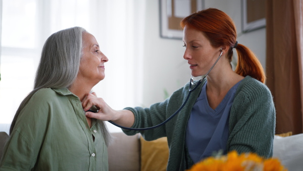 Nurse examining senior patient with stethoscope at home.