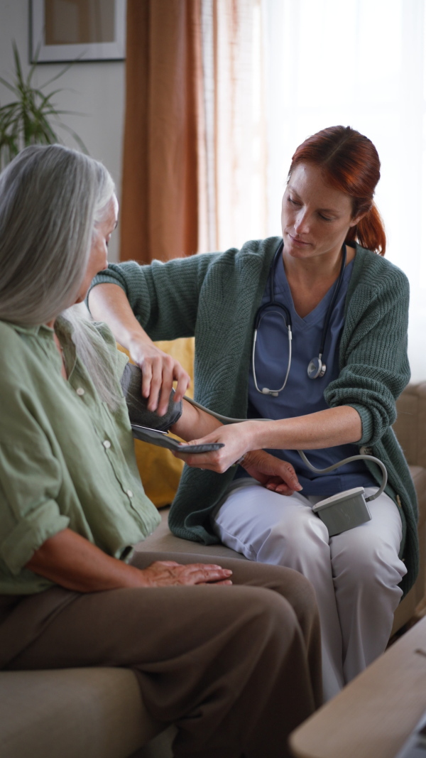 Nurse measuring blood pressuer to senior woman in her home, vertical footage.