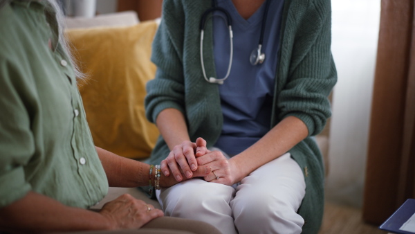 Nurse talking with senior woman, holding her hand and consoling her at her home.