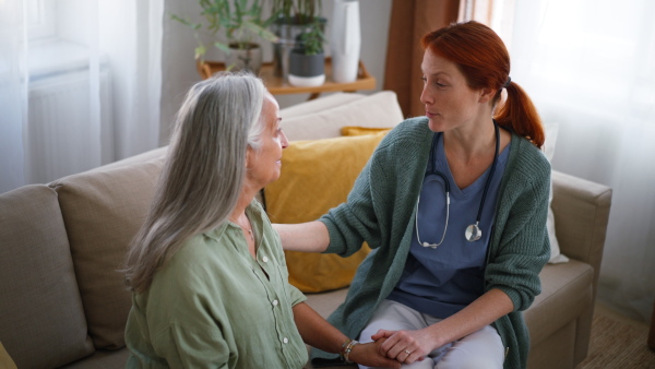 Nurse talking with senior woman, holding her hand and consoling her at her home.